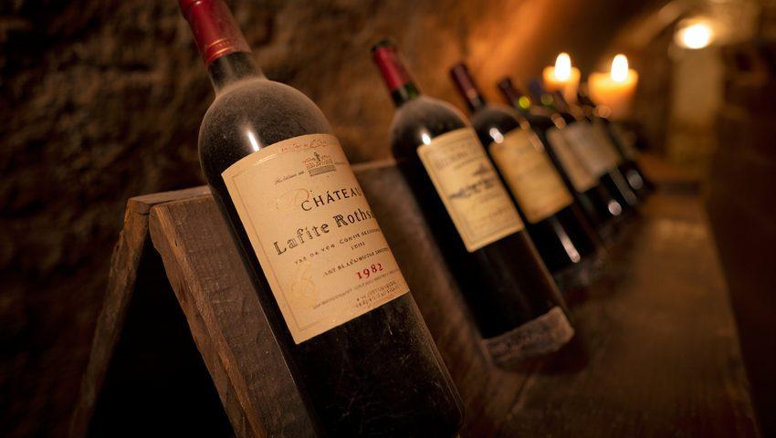 Des bouteilles millésimées alignées dans une cave voûtée en pierre, lumière ambrée et chaude