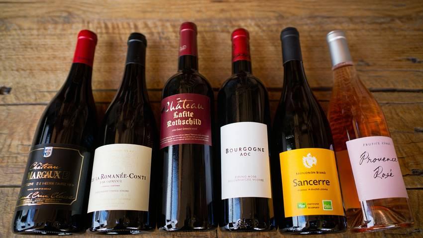 Plusieurs bouteilles de vin français avec différentes étiquettes posées côte à côte sur une table en bois, certifications et logos visibles